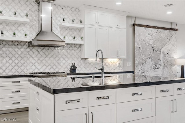 kitchen featuring sink, wall chimney range hood, stainless steel gas stovetop, decorative backsplash, and white cabinets