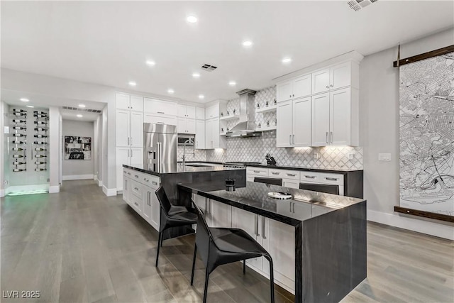 kitchen featuring stainless steel appliances, white cabinetry, wall chimney exhaust hood, and an island with sink