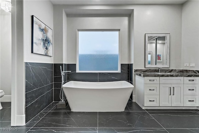 bathroom featuring a washtub, vanity, toilet, and tile walls