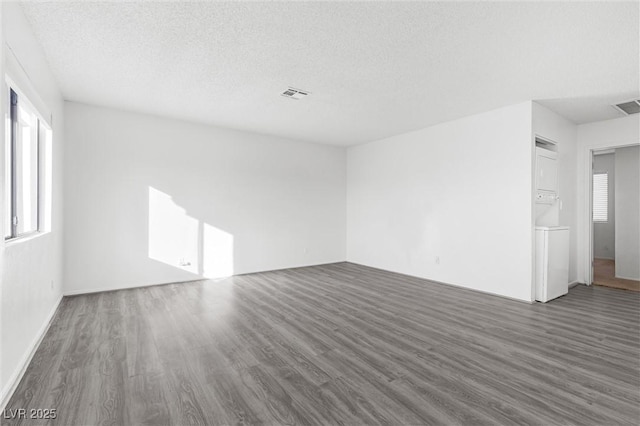 empty room featuring a textured ceiling, stacked washing maching and dryer, and dark hardwood / wood-style floors