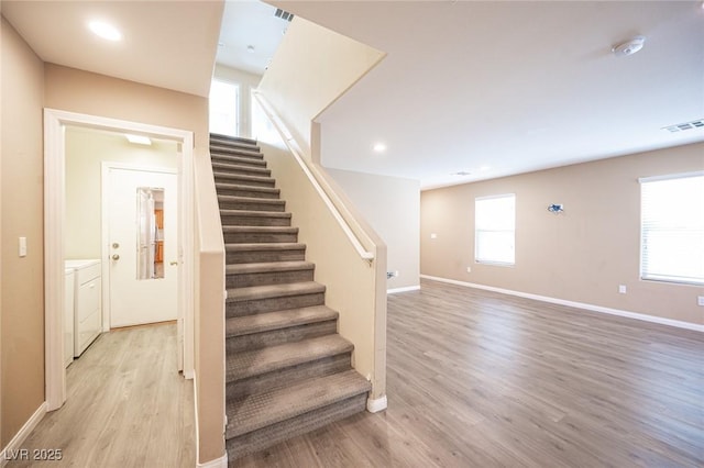 stairs featuring separate washer and dryer, a wealth of natural light, and hardwood / wood-style floors