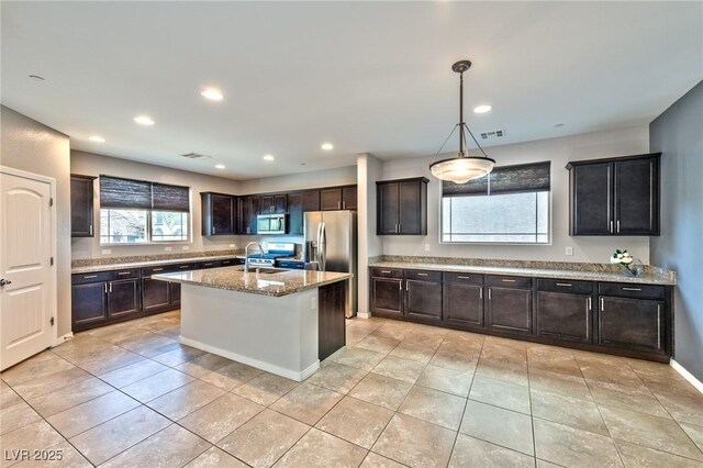 kitchen featuring light stone countertops, stainless steel appliances, decorative light fixtures, a center island with sink, and light tile patterned floors