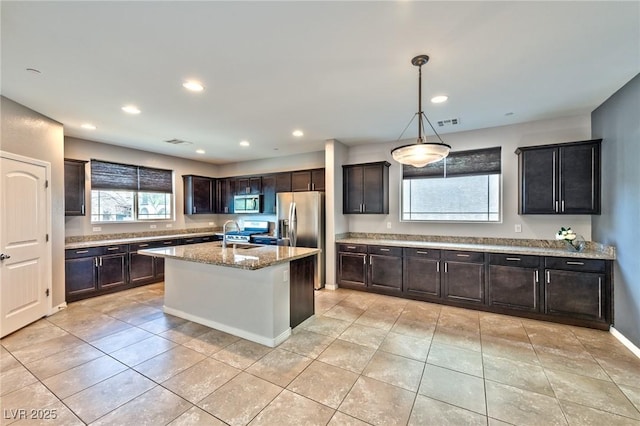 kitchen featuring light tile patterned flooring, decorative light fixtures, a kitchen island with sink, stainless steel appliances, and light stone countertops