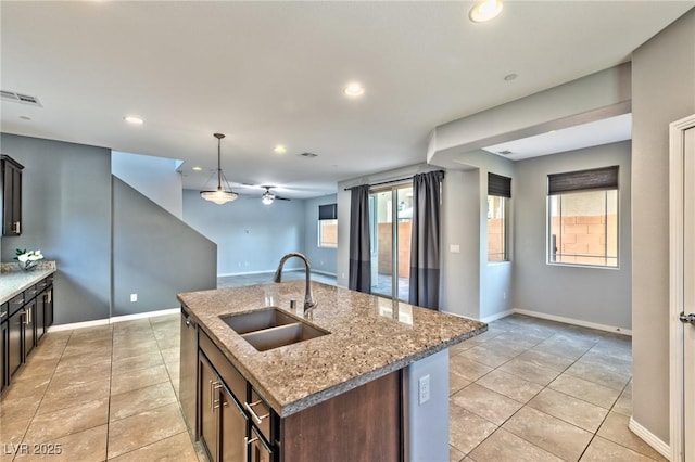 kitchen featuring light stone counters, stainless steel dishwasher, a kitchen island with sink, sink, and decorative light fixtures