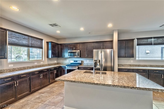 kitchen with a kitchen island with sink, sink, stainless steel appliances, and dark brown cabinetry