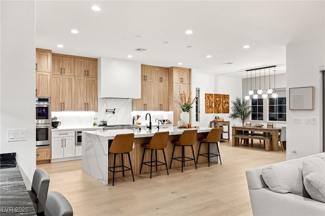 kitchen with light wood-type flooring, a breakfast bar, stainless steel appliances, a kitchen island with sink, and white cabinetry