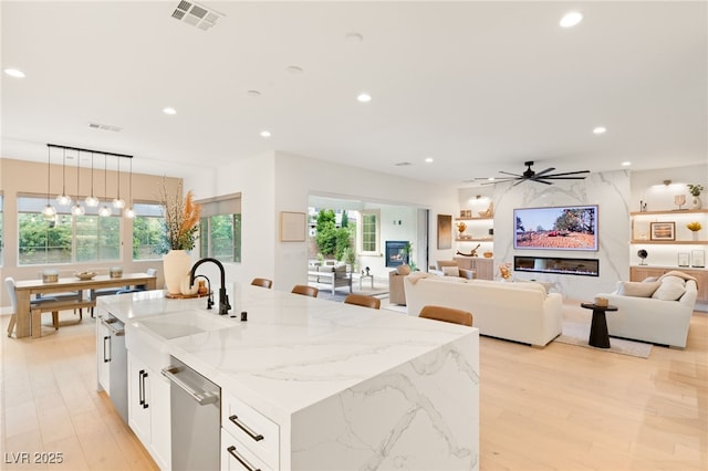 kitchen with ceiling fan, light stone countertops, an island with sink, decorative light fixtures, and white cabinetry