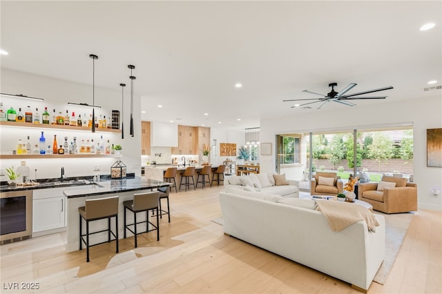 living room featuring wine cooler, ceiling fan, light wood-type flooring, and indoor wet bar