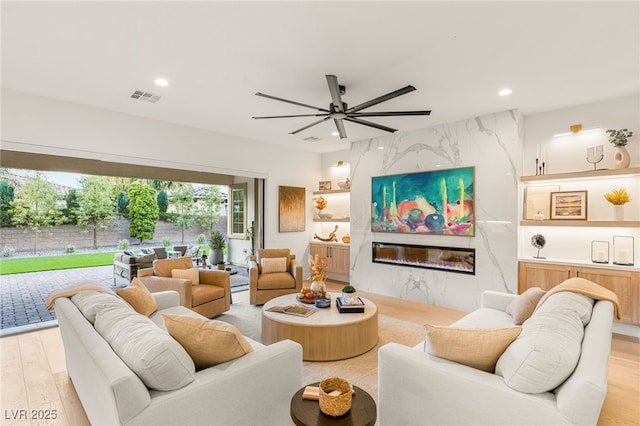 living room featuring ceiling fan, light hardwood / wood-style flooring, and a high end fireplace