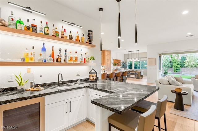 bar featuring dark stone countertops, white cabinets, light hardwood / wood-style floors, wine cooler, and hanging light fixtures