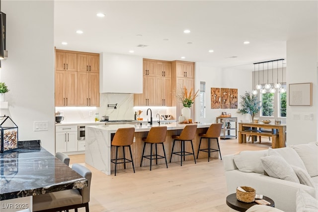 kitchen featuring premium range hood, white cabinets, a kitchen breakfast bar, tasteful backsplash, and light hardwood / wood-style floors