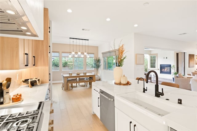 kitchen with light stone counters, sink, decorative light fixtures, dishwasher, and white cabinetry