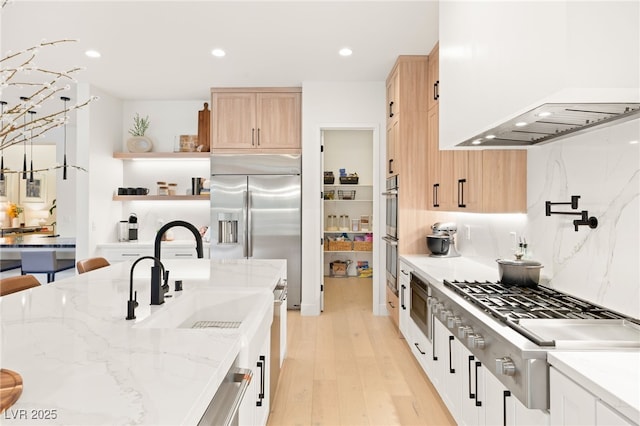 kitchen featuring white cabinets, light hardwood / wood-style flooring, wall chimney exhaust hood, light stone countertops, and stainless steel appliances