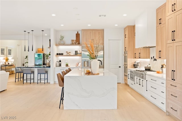 kitchen featuring appliances with stainless steel finishes, light wood-type flooring, custom range hood, decorative light fixtures, and a breakfast bar area