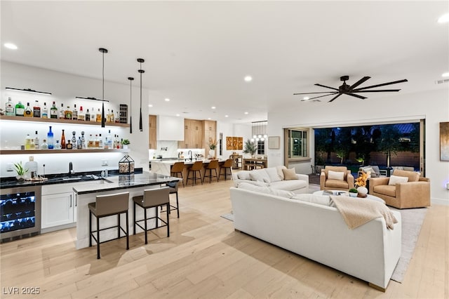 living room with light wood-type flooring, indoor bar, wine cooler, and ceiling fan