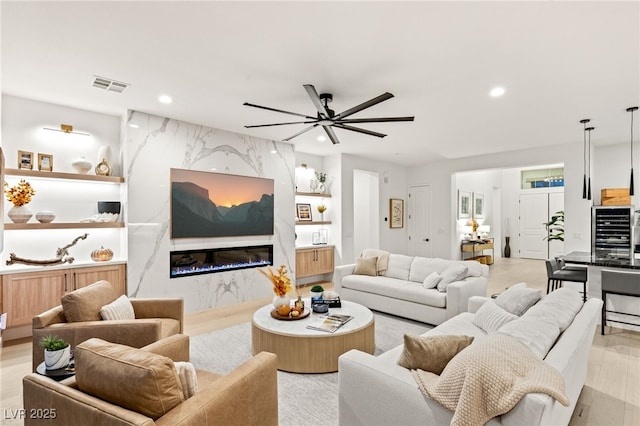 living room with a fireplace, light hardwood / wood-style floors, wine cooler, and ceiling fan