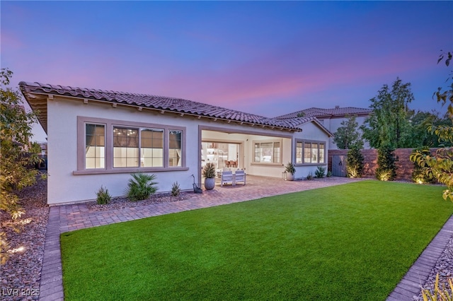 back house at dusk with a lawn and a patio area