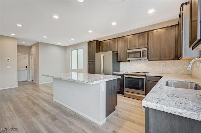 kitchen featuring a center island, sink, appliances with stainless steel finishes, tasteful backsplash, and light stone counters