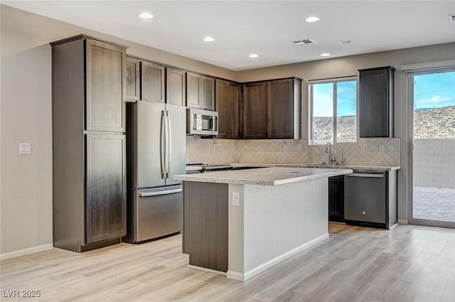 kitchen featuring a center island, tasteful backsplash, light hardwood / wood-style flooring, dark brown cabinets, and appliances with stainless steel finishes