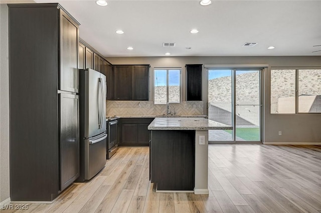 kitchen with appliances with stainless steel finishes, a kitchen island, plenty of natural light, and light stone counters