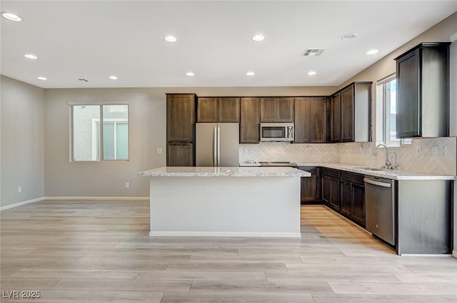 kitchen with appliances with stainless steel finishes, light stone counters, sink, light hardwood / wood-style flooring, and a center island