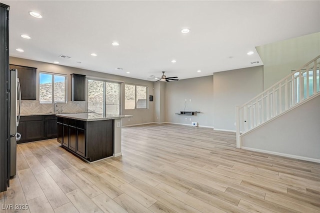 kitchen with light stone countertops, stainless steel fridge, tasteful backsplash, light hardwood / wood-style flooring, and a center island