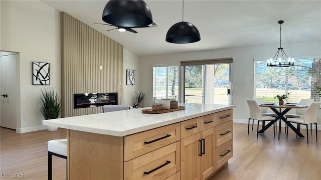 kitchen featuring pendant lighting, light wood-type flooring, a fireplace, light brown cabinetry, and a kitchen island