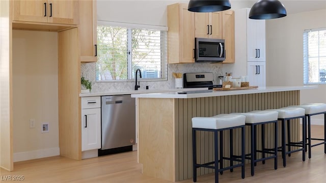 kitchen featuring decorative backsplash, appliances with stainless steel finishes, light wood-type flooring, a kitchen breakfast bar, and light brown cabinetry