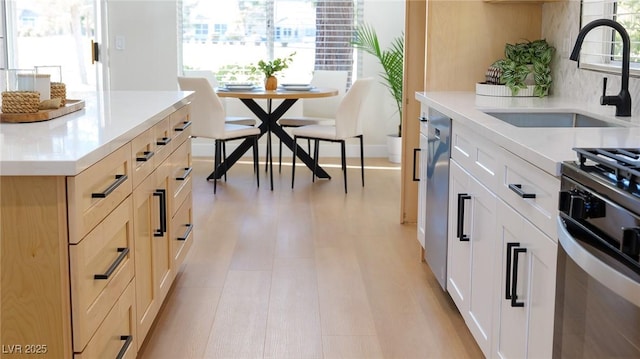 kitchen featuring backsplash, light brown cabinets, stainless steel range with gas cooktop, and sink