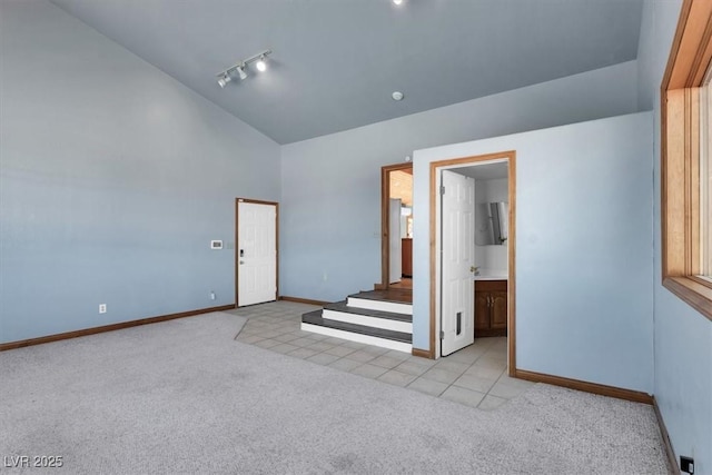 carpeted empty room with high vaulted ceiling and track lighting