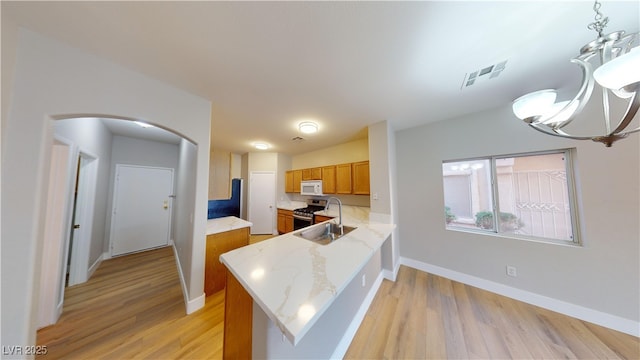 kitchen with sink, stainless steel range with gas cooktop, kitchen peninsula, decorative light fixtures, and light wood-type flooring