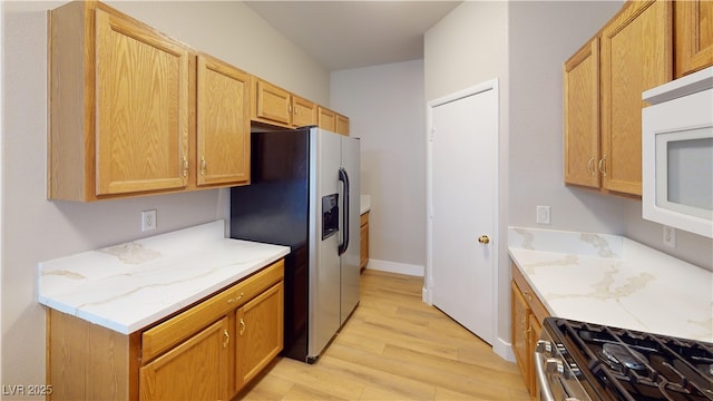 kitchen with light stone countertops, light wood-type flooring, and appliances with stainless steel finishes