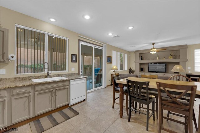 kitchen featuring dishwasher, sink, light tile patterned floors, and light stone counters