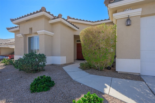 doorway to property featuring a garage, a tile roof, and stucco siding