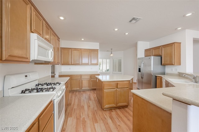 kitchen with light wood finished floors, light countertops, visible vents, a sink, and white appliances