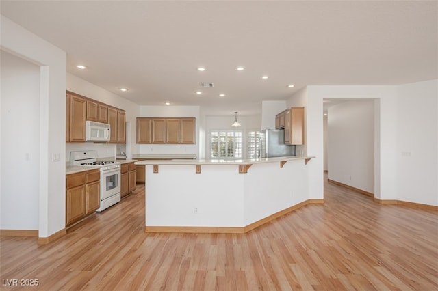 kitchen with a peninsula, white appliances, light wood-type flooring, and a breakfast bar area