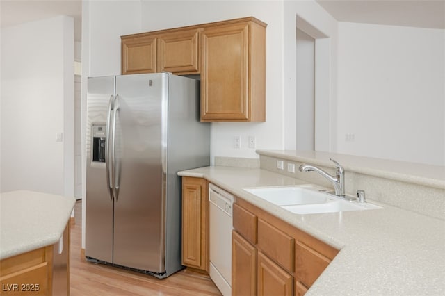 kitchen with a sink, light countertops, light wood-type flooring, dishwasher, and stainless steel fridge