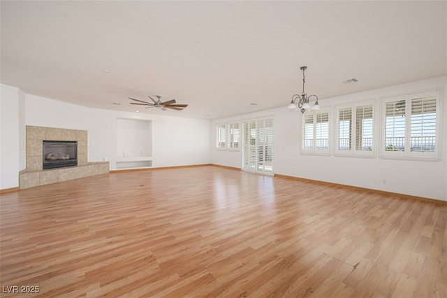 unfurnished living room with light wood finished floors, visible vents, baseboards, a tiled fireplace, and ceiling fan with notable chandelier