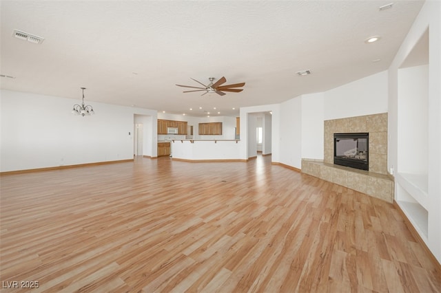 unfurnished living room with a tile fireplace, visible vents, light wood finished floors, and ceiling fan with notable chandelier