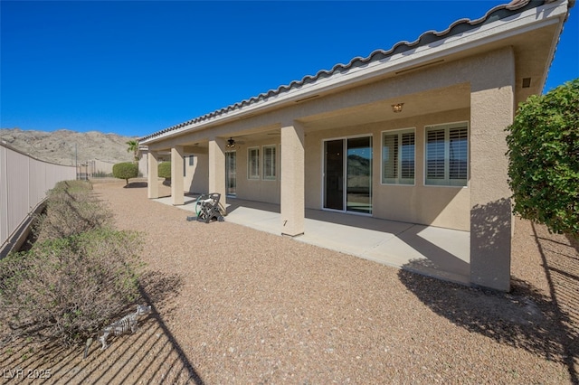 rear view of house with a mountain view, fence, a ceiling fan, stucco siding, and a patio area