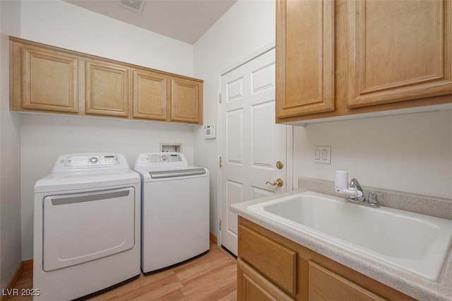 clothes washing area featuring cabinet space, visible vents, light wood-style floors, washing machine and dryer, and a sink