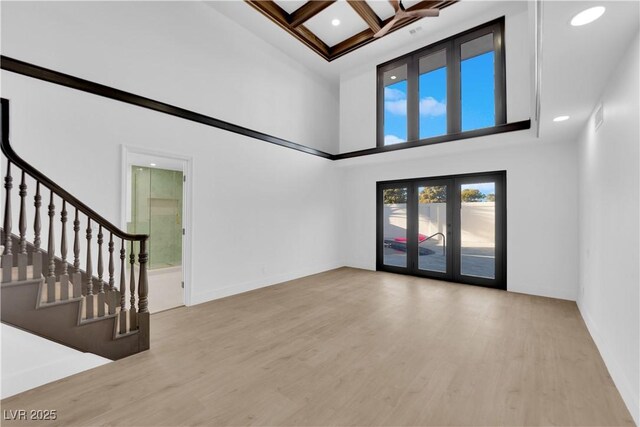 unfurnished living room with a towering ceiling, hardwood / wood-style floors, beamed ceiling, ornamental molding, and coffered ceiling