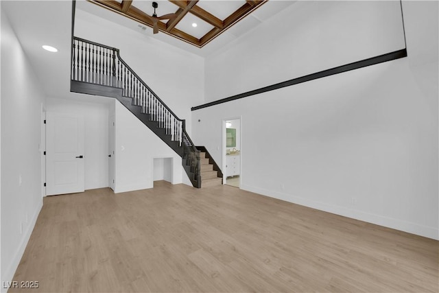 interior space with coffered ceiling, beam ceiling, a towering ceiling, and light wood-type flooring