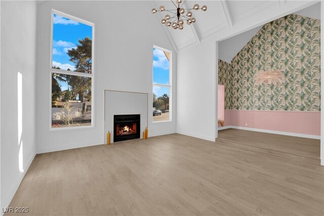 unfurnished living room featuring a notable chandelier, beam ceiling, a towering ceiling, and light wood-type flooring