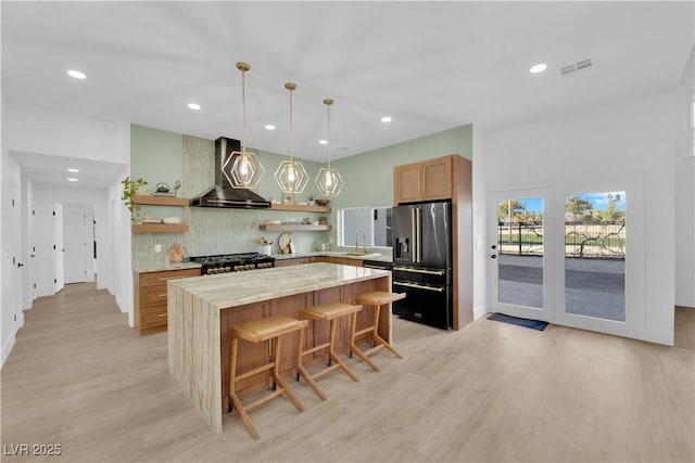 kitchen with a center island, a kitchen breakfast bar, wall chimney range hood, decorative backsplash, and appliances with stainless steel finishes