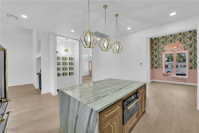 kitchen with pendant lighting, light hardwood / wood-style flooring, light stone counters, a notable chandelier, and stainless steel oven