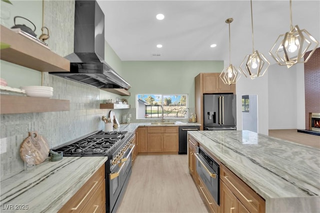 kitchen featuring wall chimney exhaust hood, light stone counters, premium appliances, a fireplace, and decorative backsplash