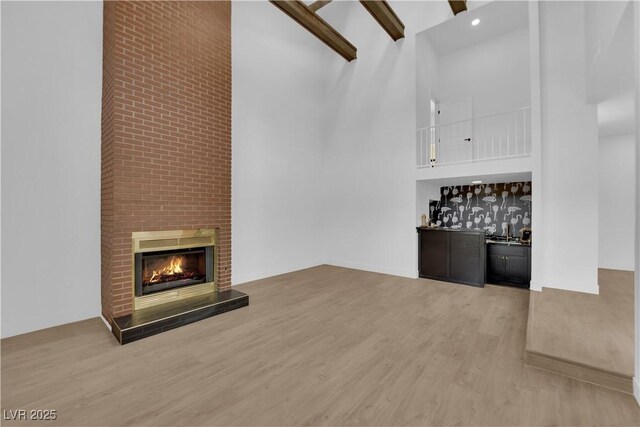 unfurnished living room featuring a brick fireplace, hardwood / wood-style flooring, high vaulted ceiling, and beamed ceiling