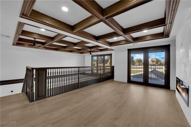 empty room with coffered ceiling, light hardwood / wood-style floors, beam ceiling, and a wealth of natural light