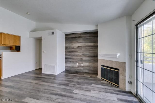 unfurnished living room with hardwood / wood-style flooring, lofted ceiling, and a tiled fireplace